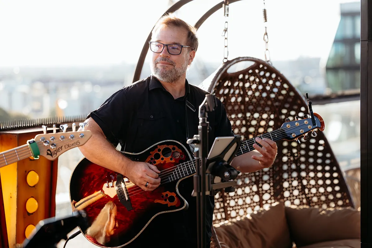 Gitarrist Andrés von Time Is Now mit Akustikgitarre auf einer Dachterrasse